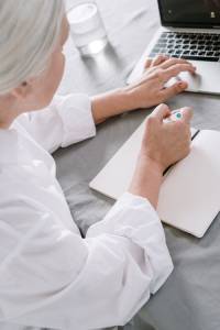 Person writing in notebook and on laptop, medical transcription